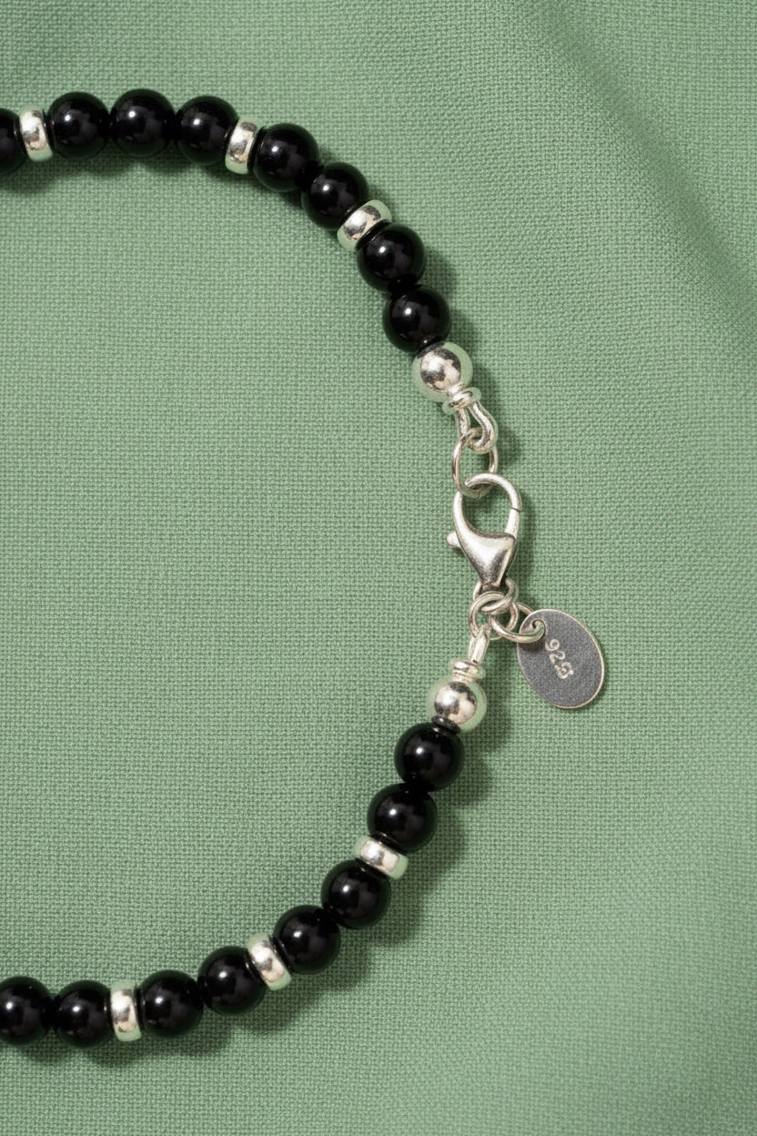 Black tourmaline beaded bracelet with silver accents on a green fabric background