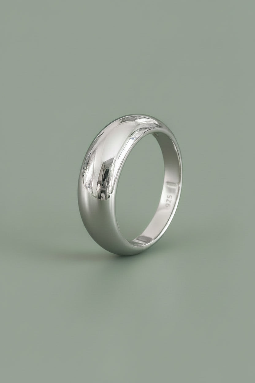 A polished sterling silver ring broad across the top and tapers to a thinner width on the bottom, shown against a solid sage green background.