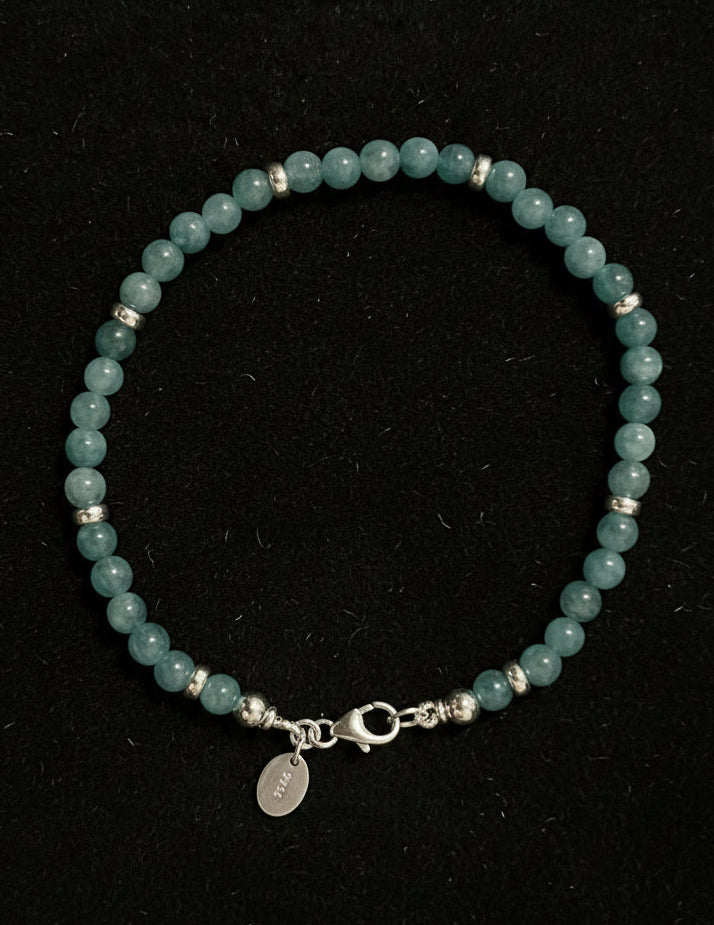 Cyan coloured jade beaded bracelet with a silver clasp on a black background