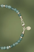 Cyan coloured jade beaded bracelet with silver clasp and silver rondelles on a green background 