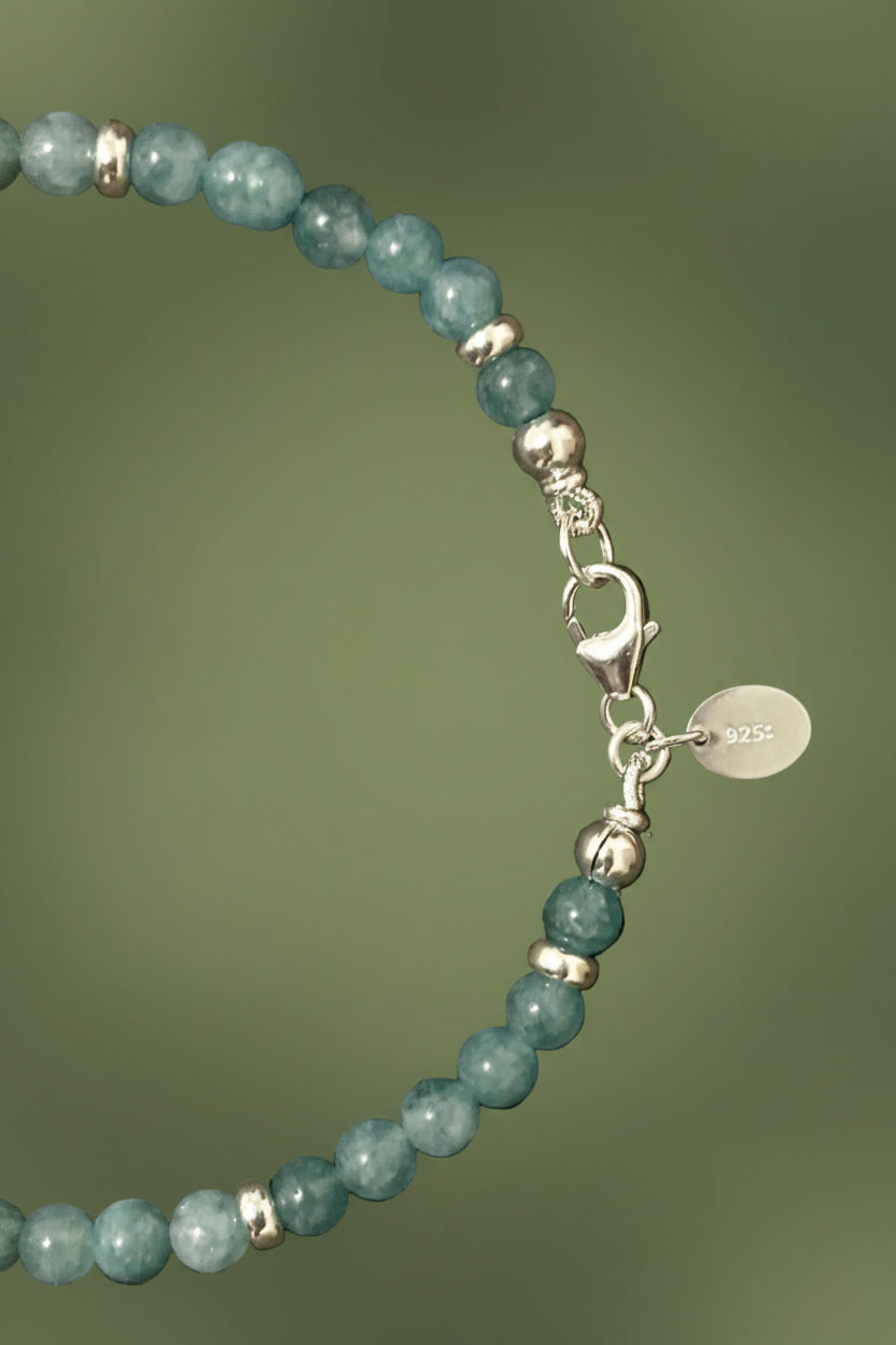 Cyan coloured jade beaded bracelet with silver clasp and silver rondelles on a green background 
