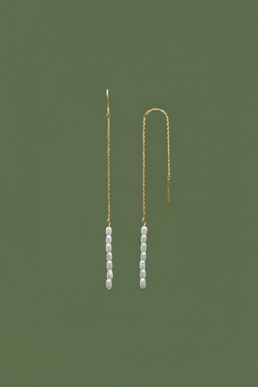 A pair of long gold-plated thread earrings with small freshwater pearls, shown against a solid olive green background.