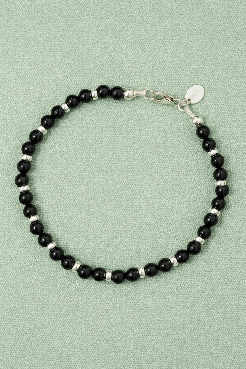 Black tourmaline and silver beaded bracelet on a light green background with silver clasp and tag