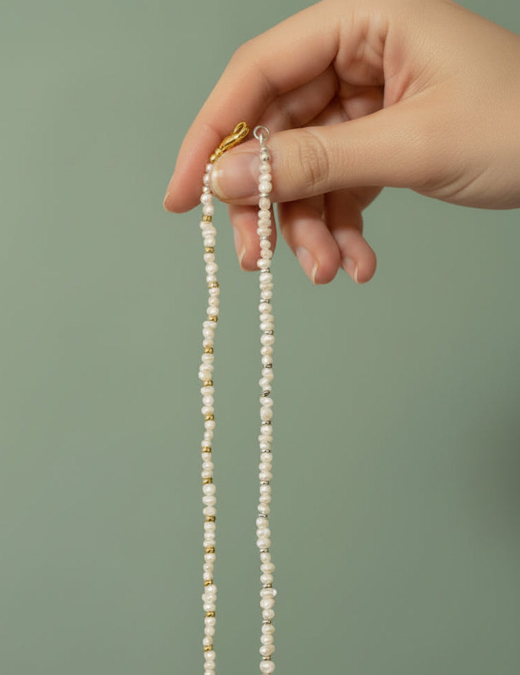 Hand holding one freshwater pearl bracelet with gold findings and another bracelet with silver findings