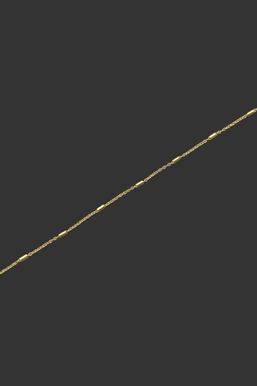 A delicate gold-plated chain bracelet laid diagonally across a plain light gray background.